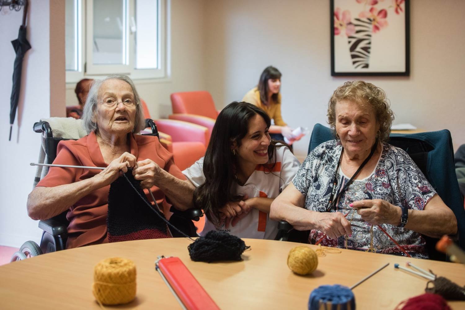 KORIAN Pressebild: Lächelnde Pflegerin mit glücklichen Senioren in einem Aufenthaltsraum in einem Pflegeheim
